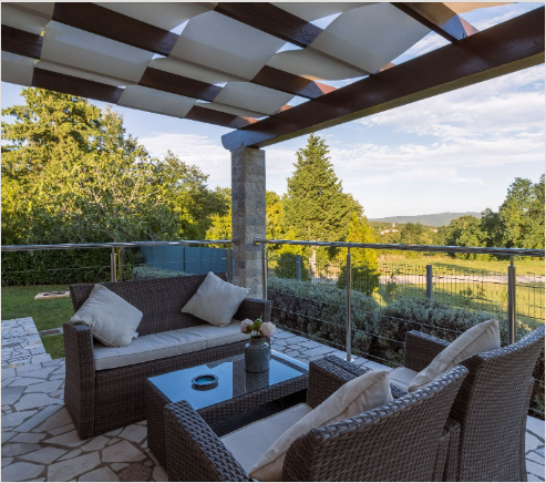 Luxury covered patio with comfortable outdoor sofa and a view of a lush landscape.