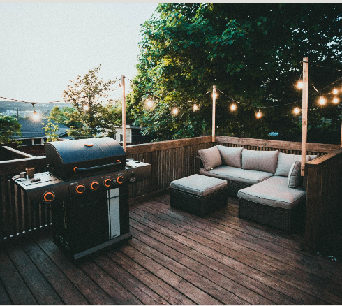 Modern dark-stained wooden deck with a BBQ grill and string lights, perfect for entertaining.