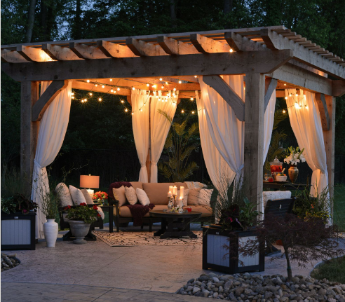 Cozy backyard pergola illuminated by warm string lights at dusk, with elegant white curtains.