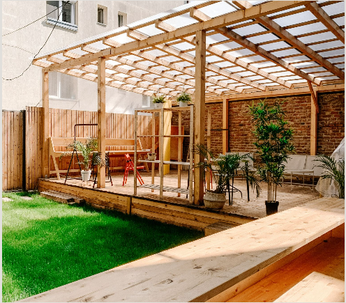 Attached wooden pergola with a clear polycarbonate roof over a backyard patio and lawn.